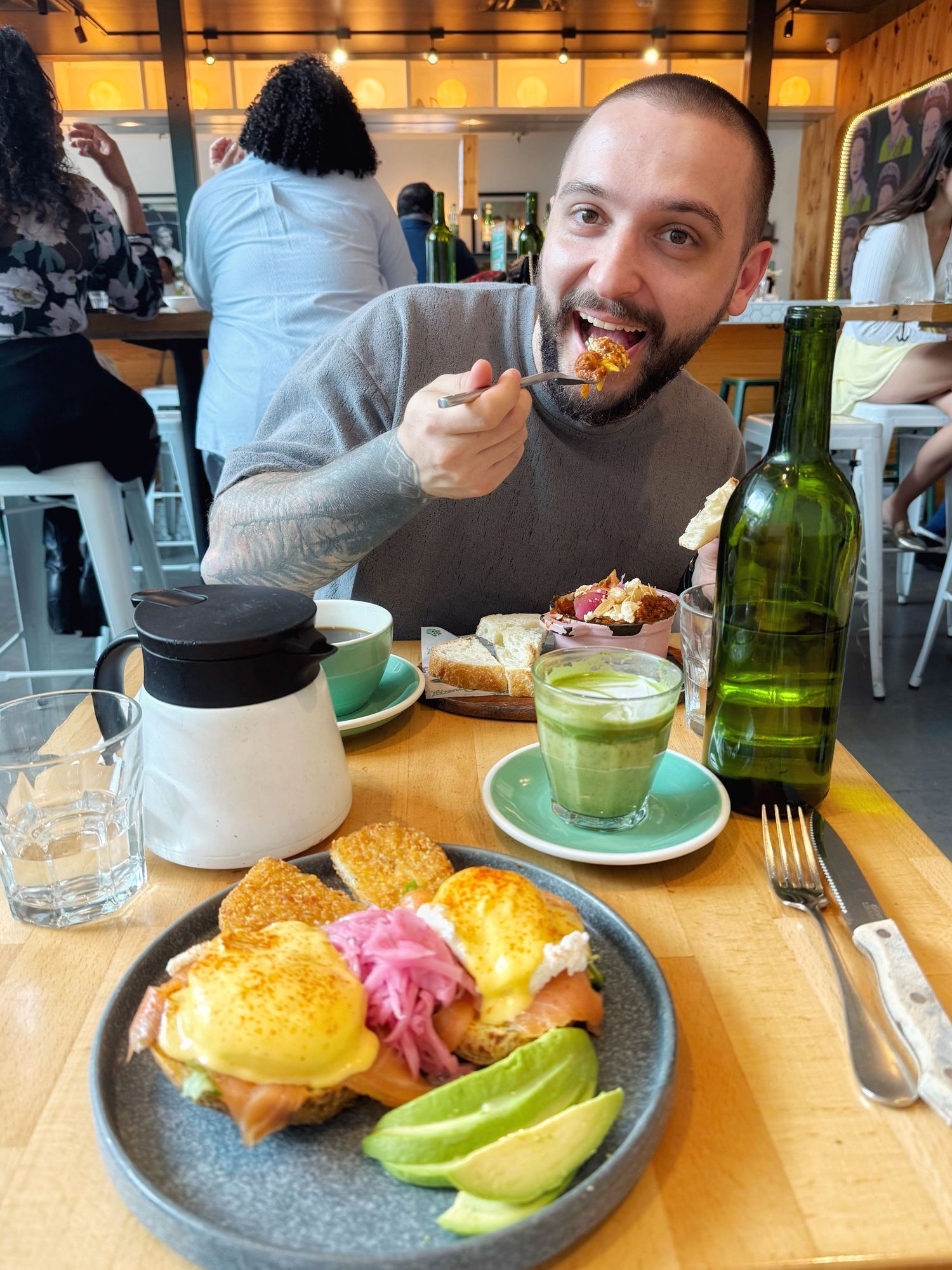 Someone enjoying brunch with eggs benedict topped with pink hollandaise sauce, avocado, and matcha drinks at a casual restaurant.