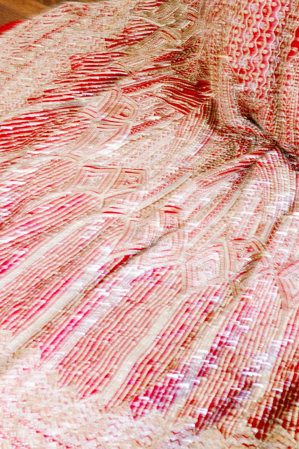 Close-up detail of intricate red and pink embroidered fabric with geometric patterns.