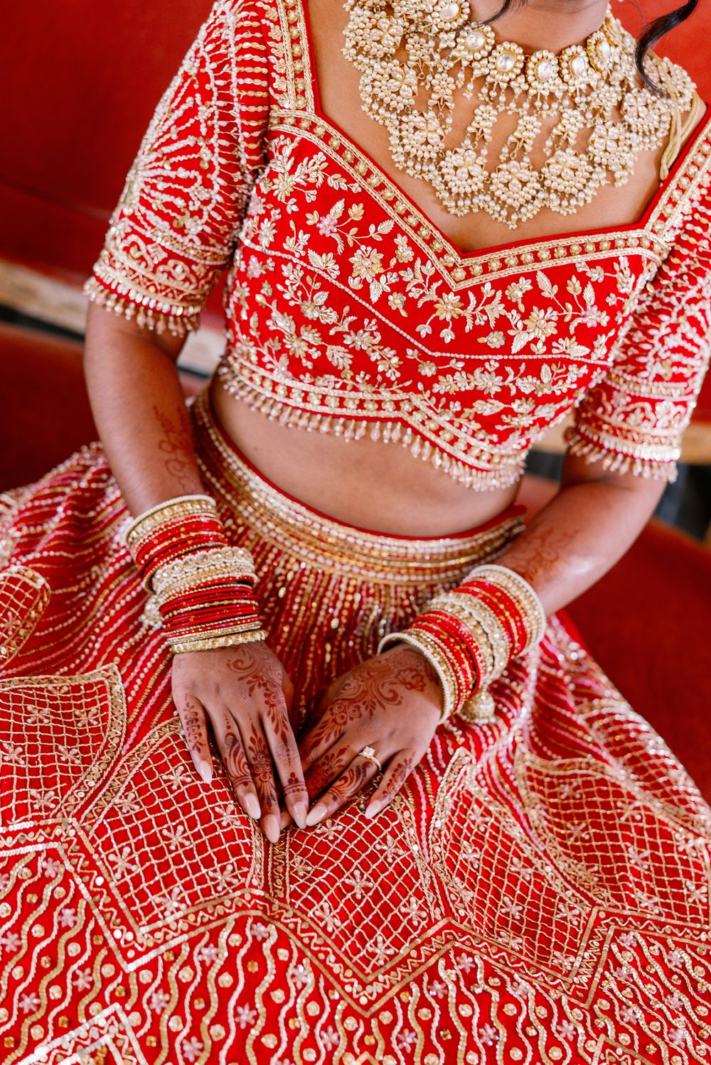 Traditional red and gold Indian bridal lehenga with intricate beadwork and bangles shown in a detailed close-up shot.
