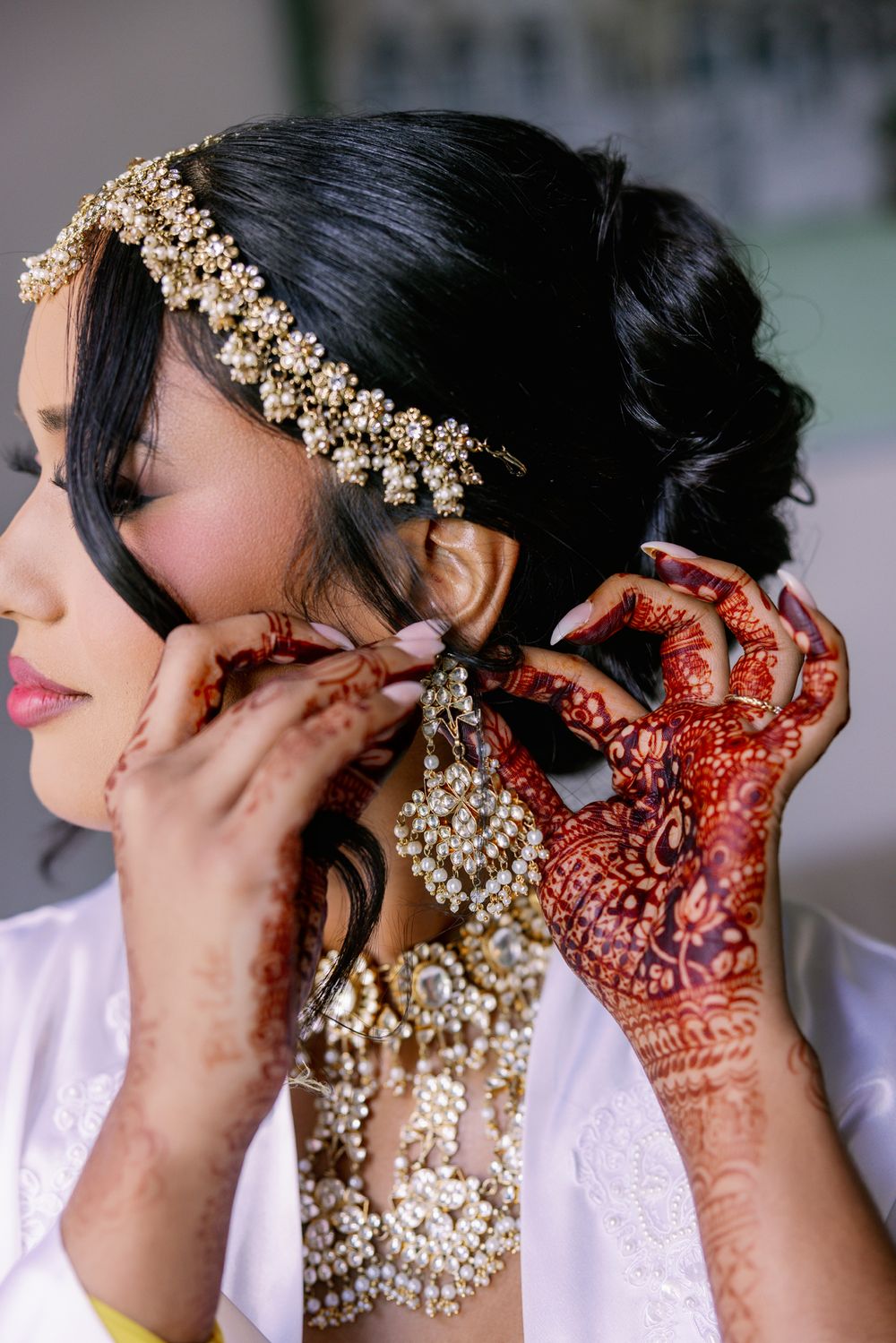 Traditional Indian bridal preparation shows intricate mehndi designs on hands and pearl jewelry being put on for wedding ceremony.