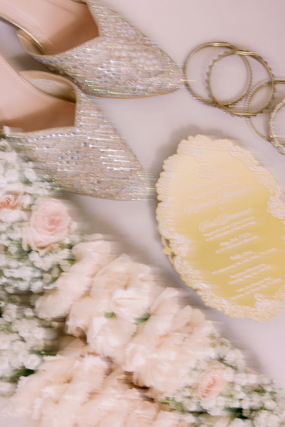 Delicate bridal accessories including lace details, gold bangles, and soft pink roses arranged on a light surface.