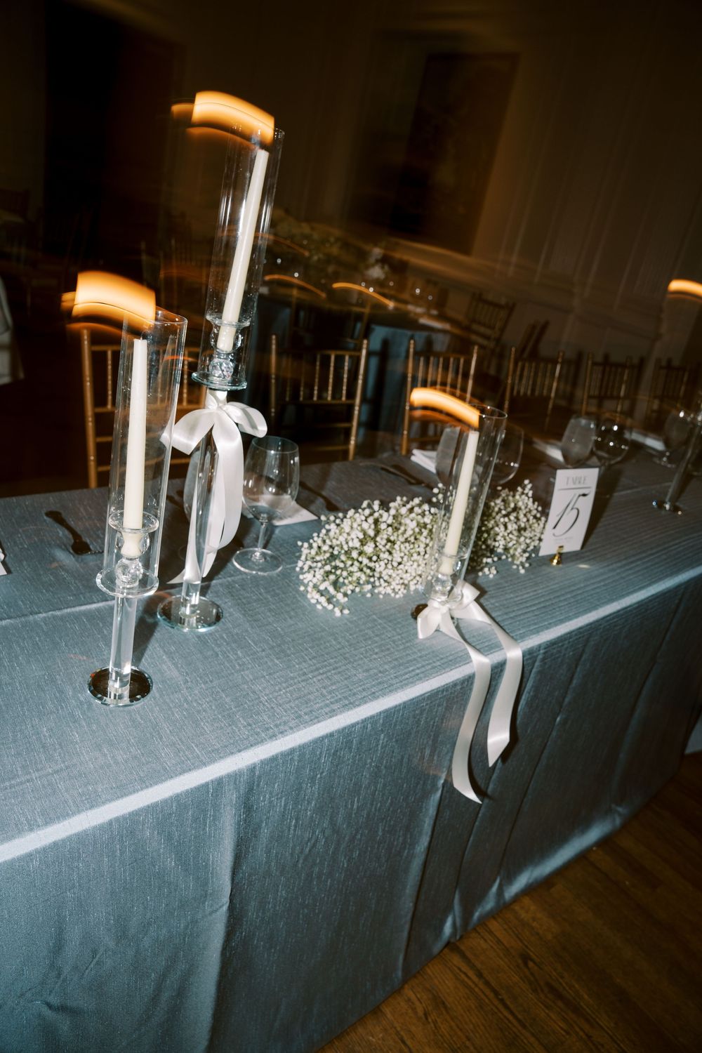 Wedding table decor featuring tall glass candle holders with white ribbons and baby's breath flowers. NC WEDDING PHOTOGRAPHER, LUXURY WEDDIN