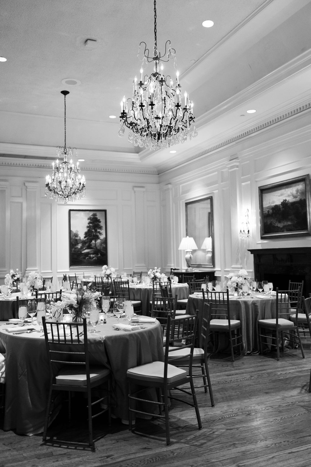 Formal wedding reception room with crystal chandeliers and round tables set with dark linens. NC WEDDING PHOTOGRAPHER, LUXURY WEDDING PHOTOG