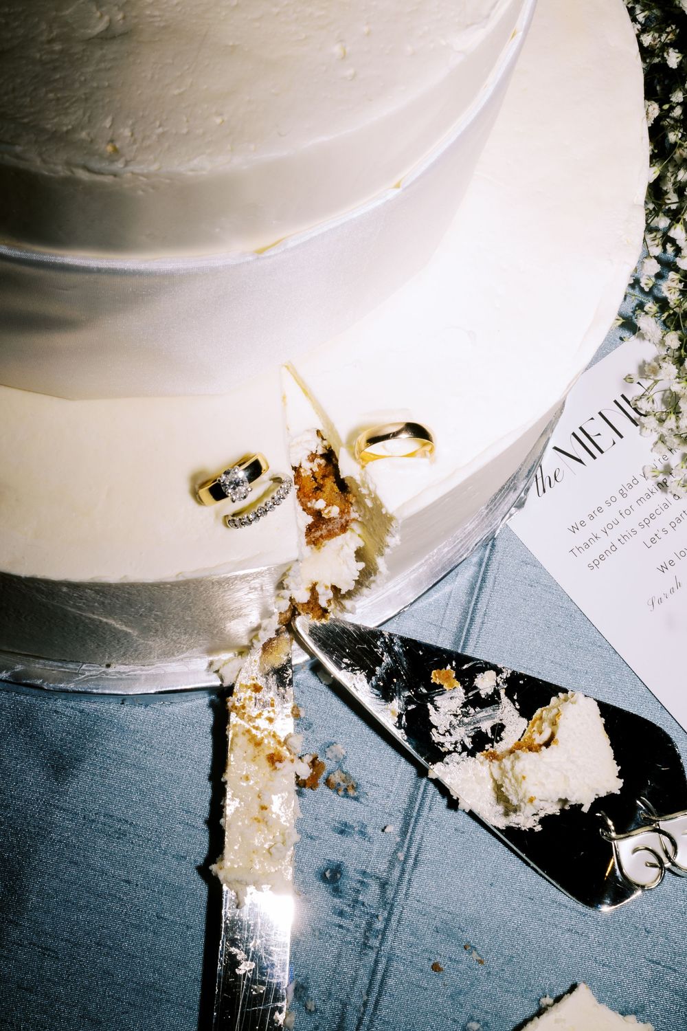 Close-up of wedding rings and cake slice on an invitation with white frosting. NC WEDDING PHOTOGRAPHER, LUXURY WEDDING PHOTOGRAPHER