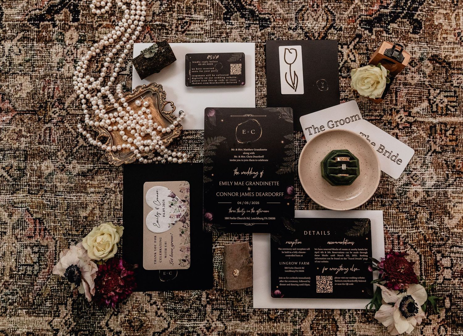 Romantic wedding flat lay with invitation suite, pearl necklace, florals, place cards, RSVP, and green velvet ring box on vintage rug.