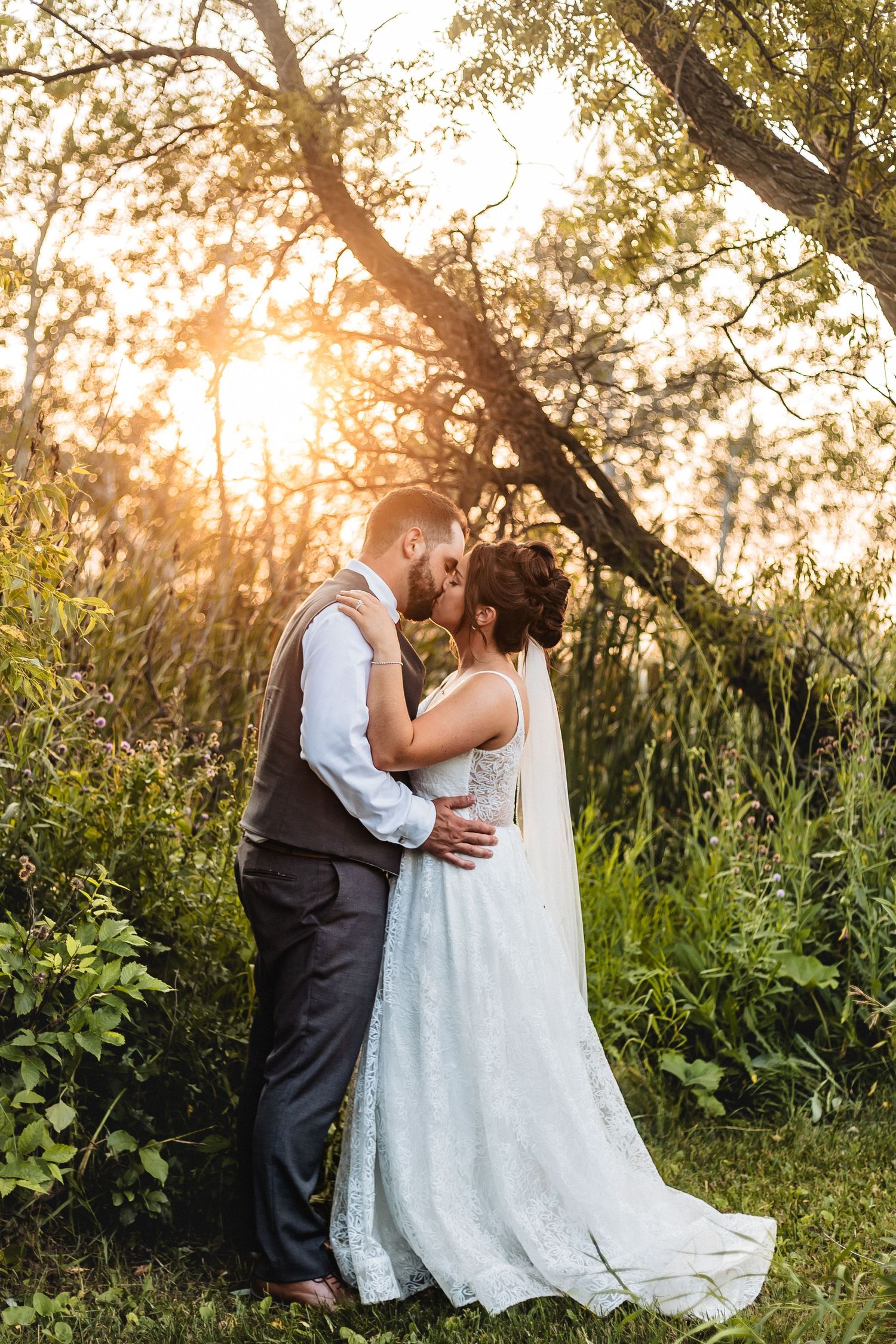 A romantic sunset wedding portrait showing a couple embracing outdoors with golden sunlight filtering through trees.