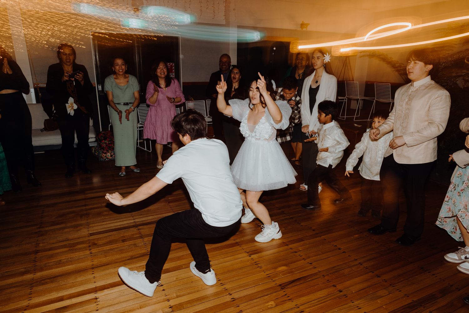 Dynamic dance moves at a wedding reception with onlookers cheering around the dance floor.