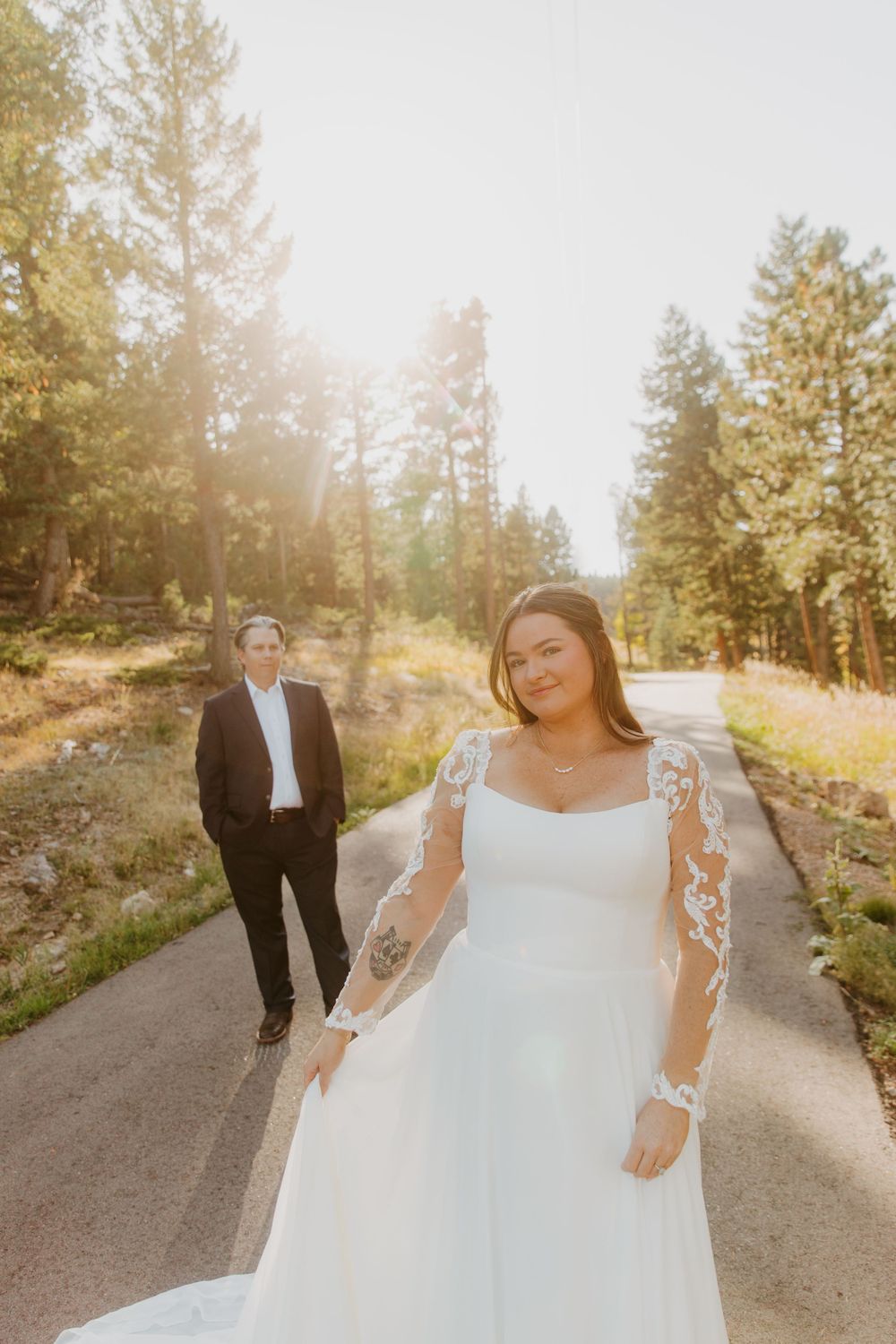 Golden sunlit forest path with wedding couple in white dress and black suit creating a romantic outdoor scene in Denver, Colorado.