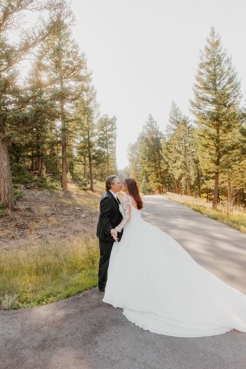 A couple shares a romantic moment on a winding forest road surrounded by tall pine trees at sunset in Denver, Colorado.