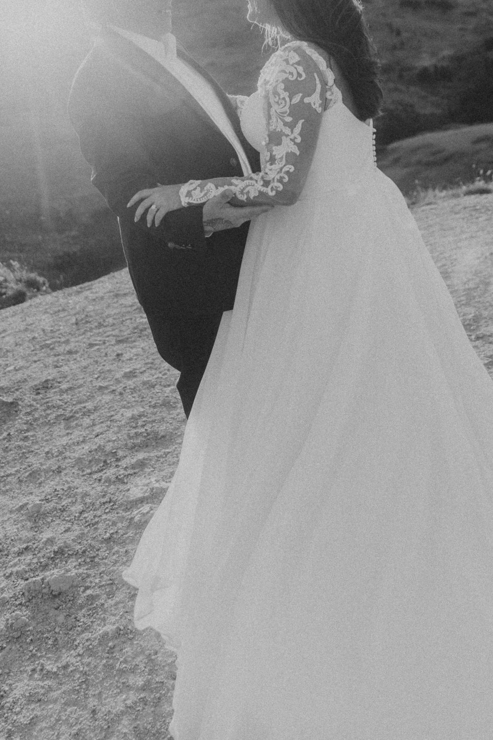 A black and white wedding photo showing a bride in a lace sleeve gown embracing someone on a hillside in Denver, Colorado.