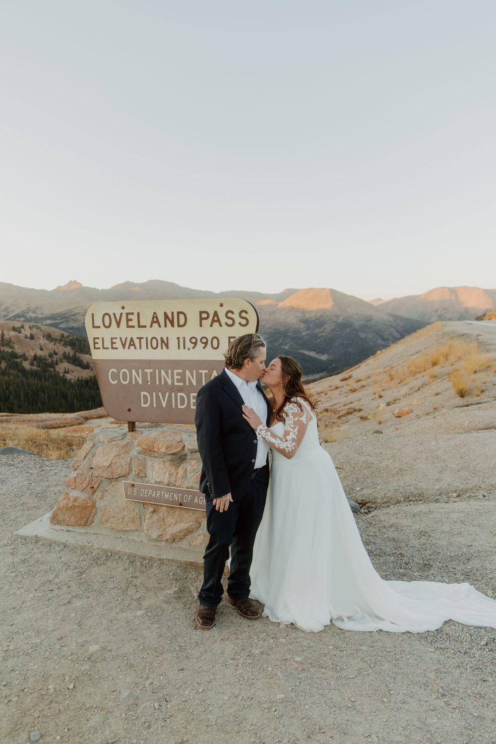 A couple shares a romantic moment at the Loveland Pass Continental Divide sign during sunset in Colorado.