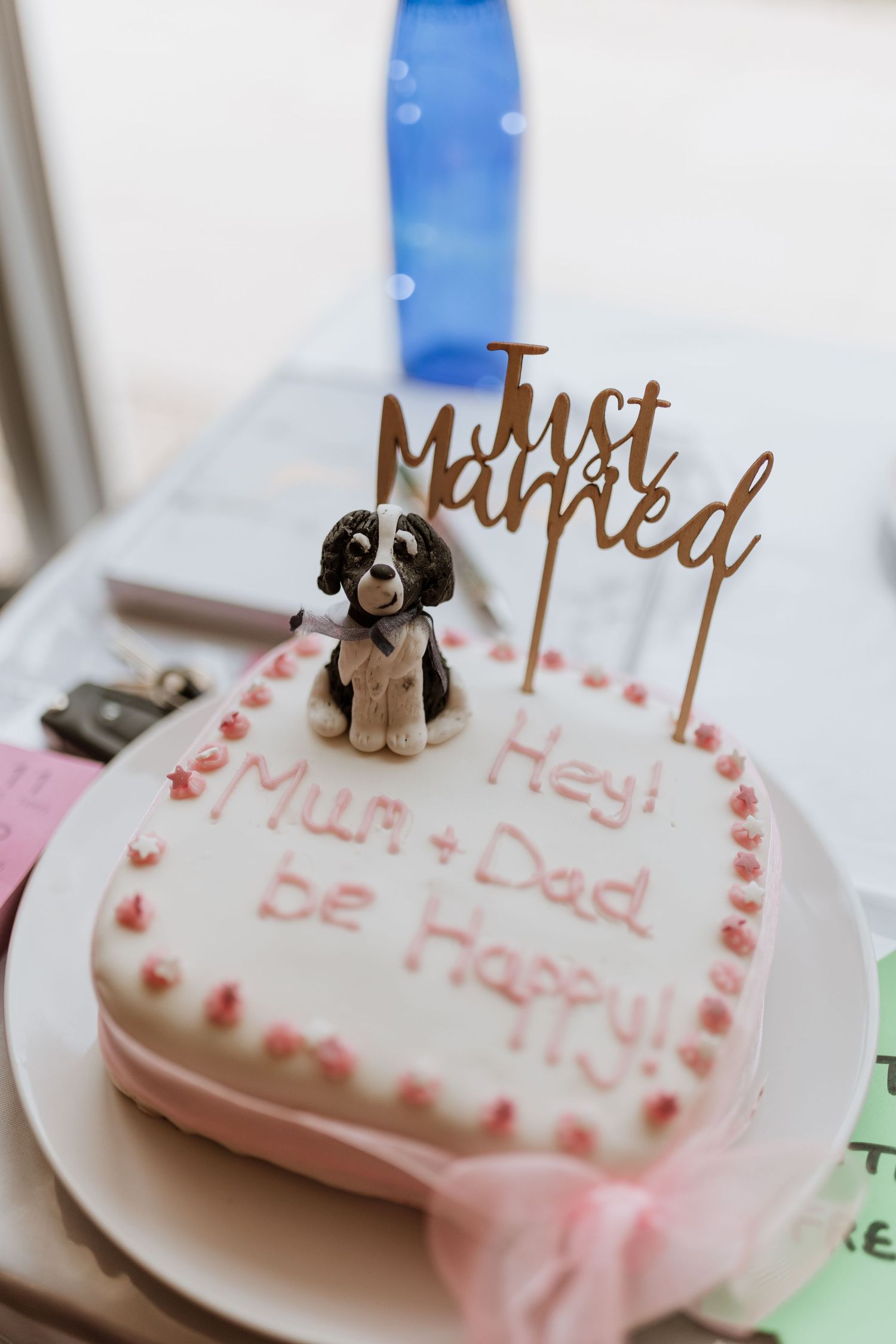 A heart-shaped pink cake with 'Just Married' topper and small dog figurine celebrating a couple's special day.