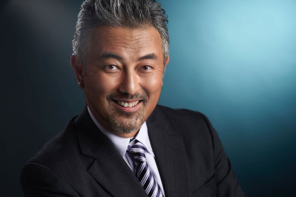 Professional headshot of Kazuhiro Kumochi in business attire against a teal backdrop photographed by Evan Will of Sharko Studios