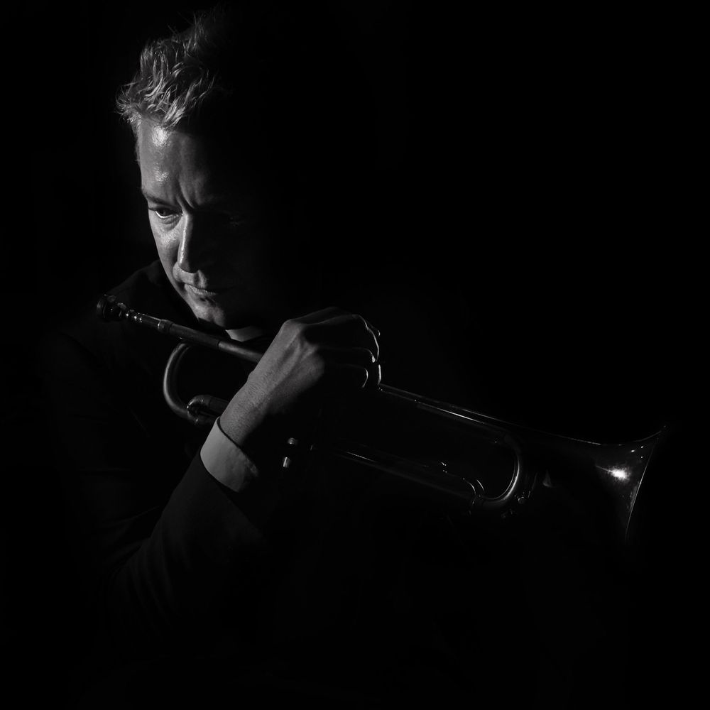 Dramatic black and white photo of trumpet player Chris Botti holding instrument in dark moody lighting photographed by Evan Will of Sharko
