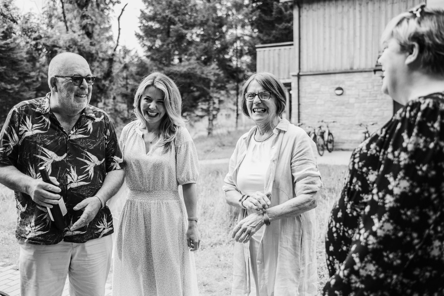 A happy bridal party converses and laughs together outdoors in black and white.