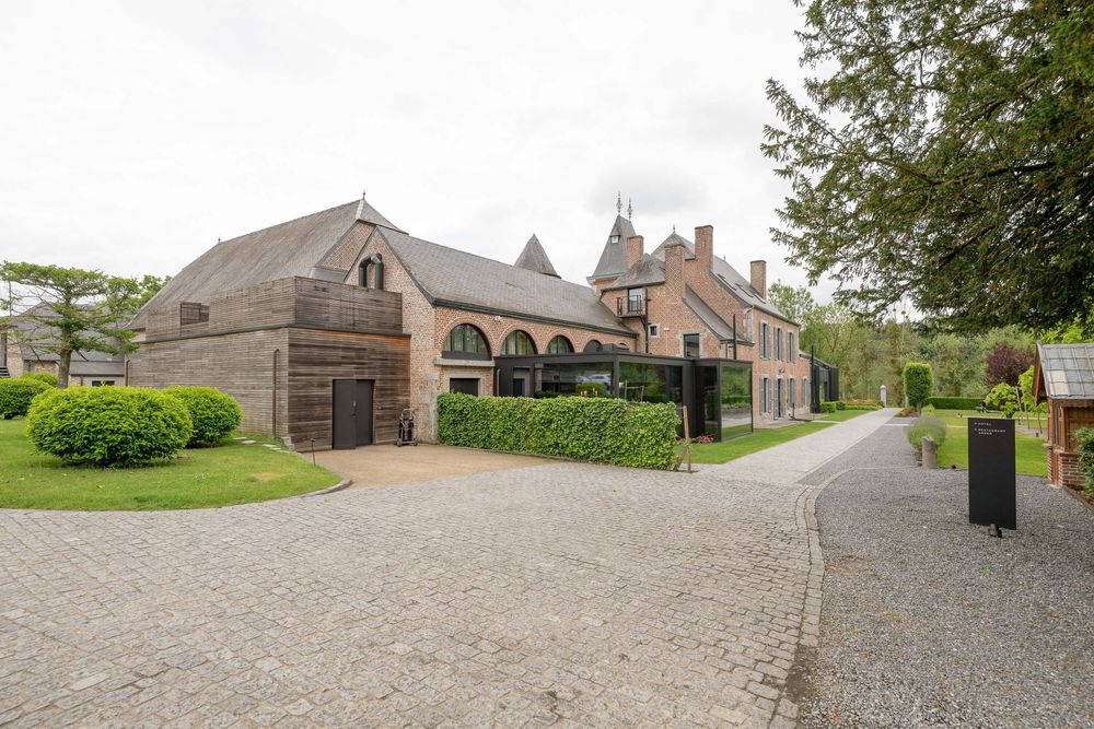 Historic brick carriage house building with arched windows and cobblestone driveway surrounded by manicured hedges and trees.