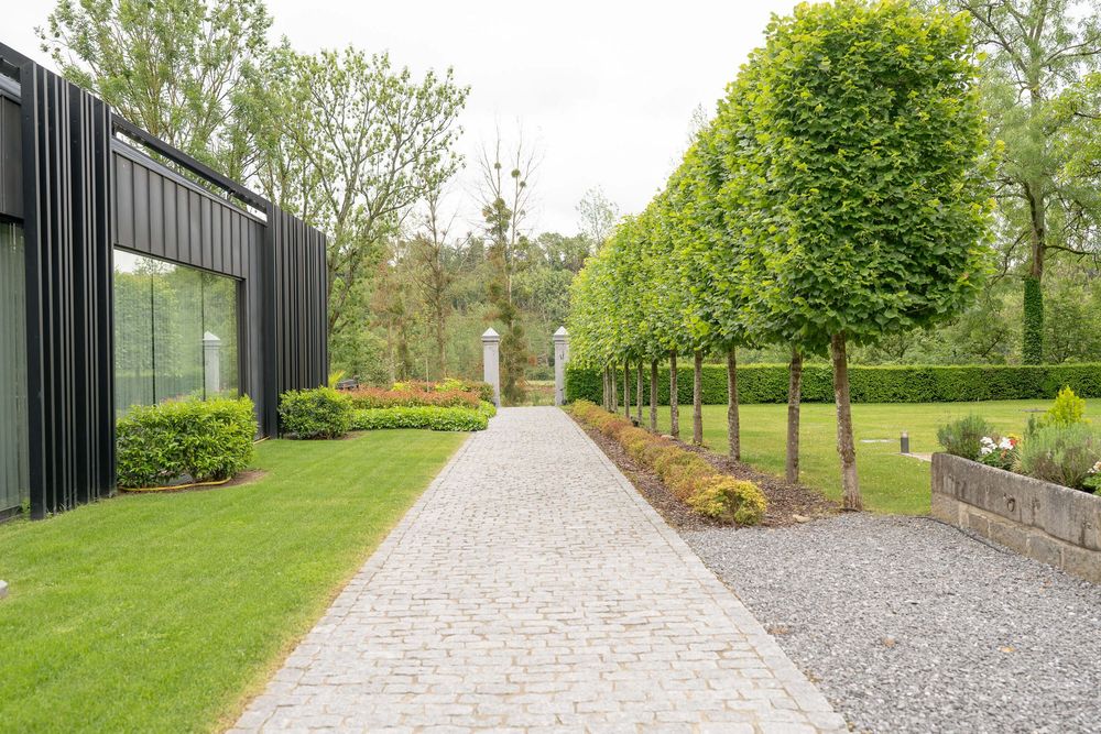 A modern garden path with gravel and paving stones leads between manicured hedges and green lawns.