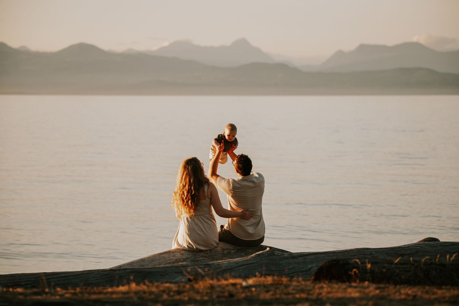 Beautiful photo of parents holding baby in the air at Neck Point Park Nanaimo with mountains family photography by Comox Valley photographer