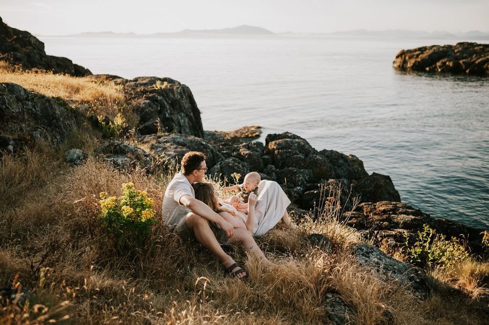 Photo of family sitting on rocky bluff grass Neck Point Park Nanaimo during golden hour family photography by Vancouver Island photographer