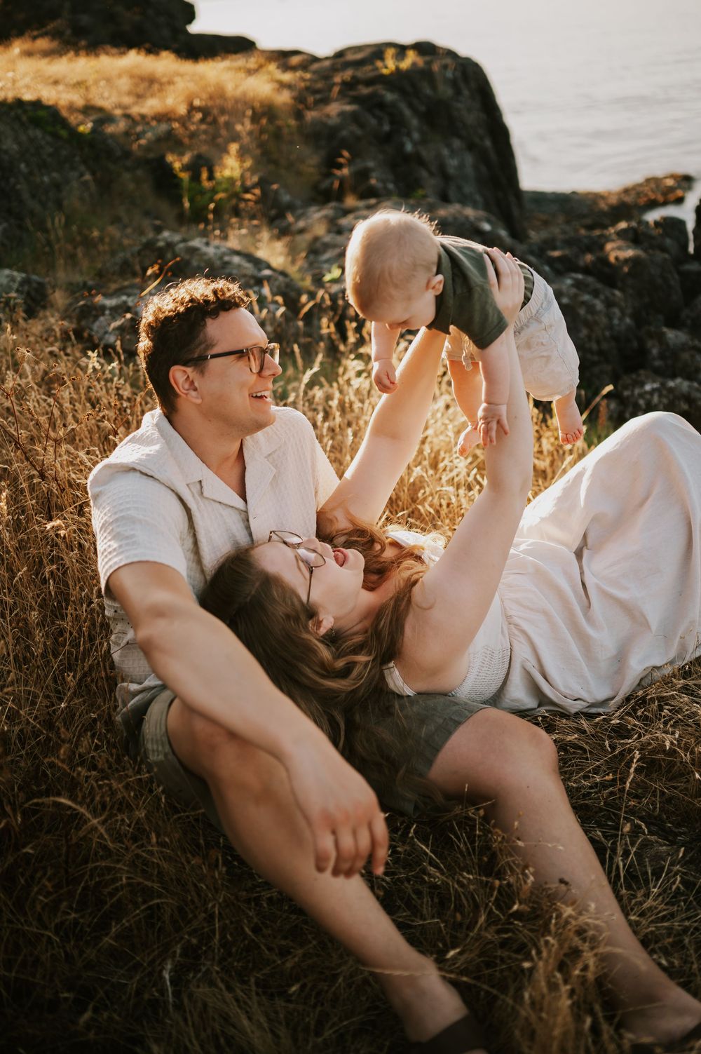 Candid photo of family holding baby rocky bluff grass Neck Point Park Nanaimo sunset family photography by Vancouver Island photographer