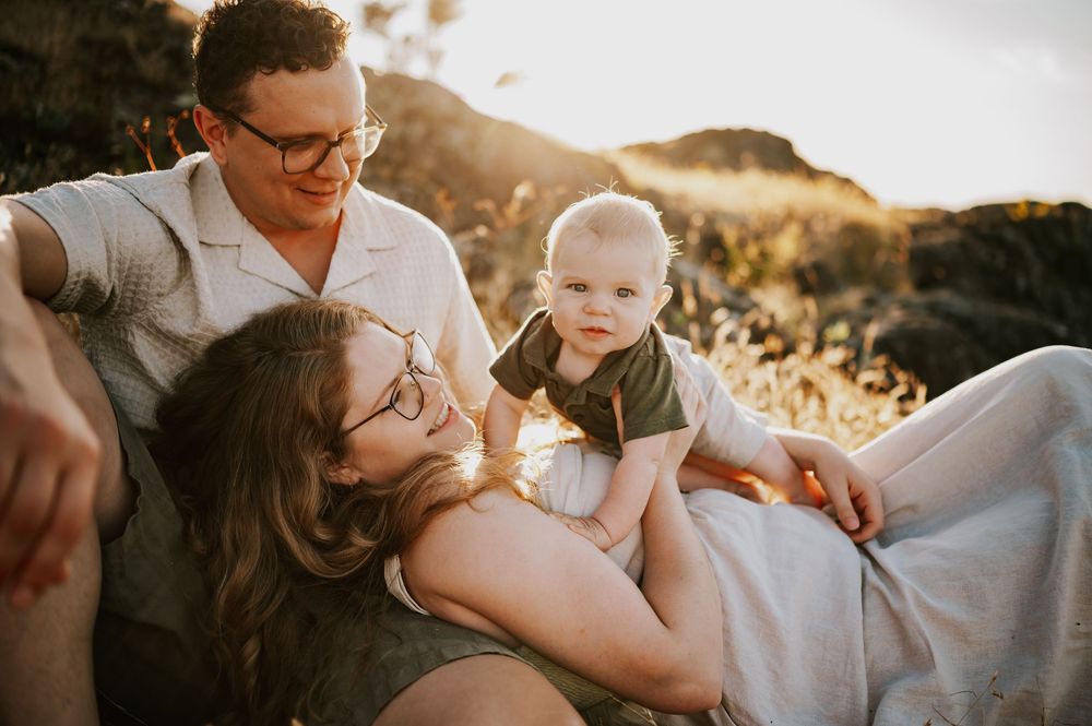 Candid photo of family sitting with baby on rocky bluff Neck Point Park Nanaimo sunset family photography by Vancouver Island photographer