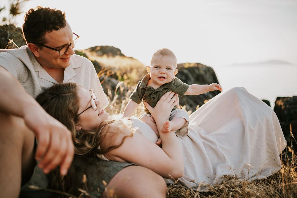Candid photo of family sitting with baby in bluff grass Neck Point Park Nanaimo sunset family photography by Vancouver Island photographer