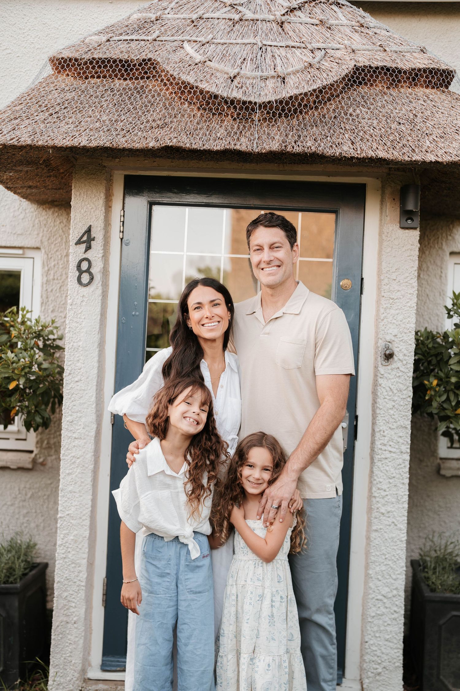 Family poses together outside a charming thatched-roof cottage entrance.