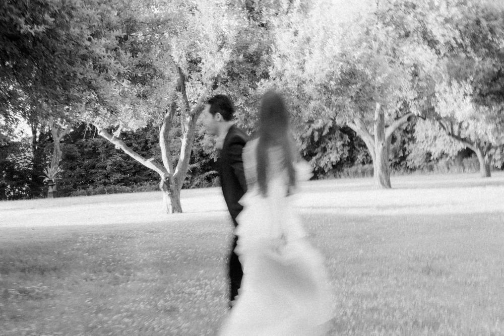A black and white motion-blurred photo of a couple in formal wedding attire standing in a garden setting.
