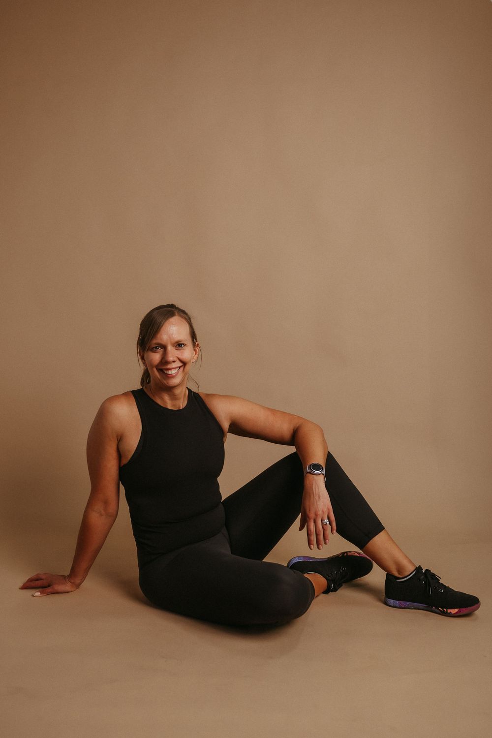 Athletic person in black activewear posing on a beige seamless backdrop in a relaxed reclining position.