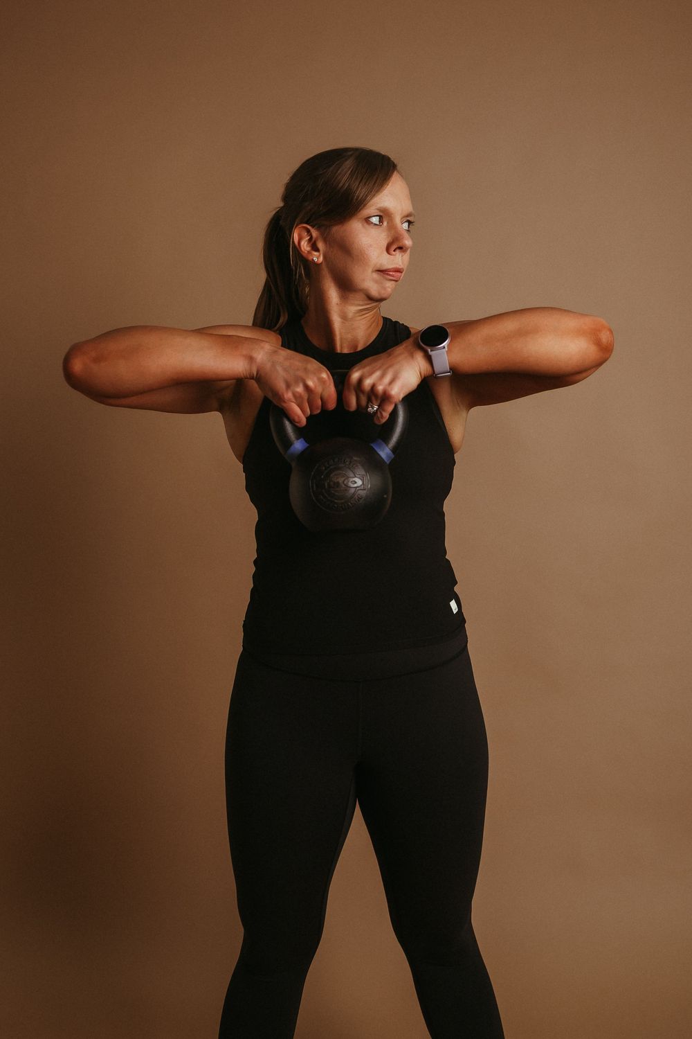Athletic person in black workout attire performing a kettlebell exercise against a brown background.