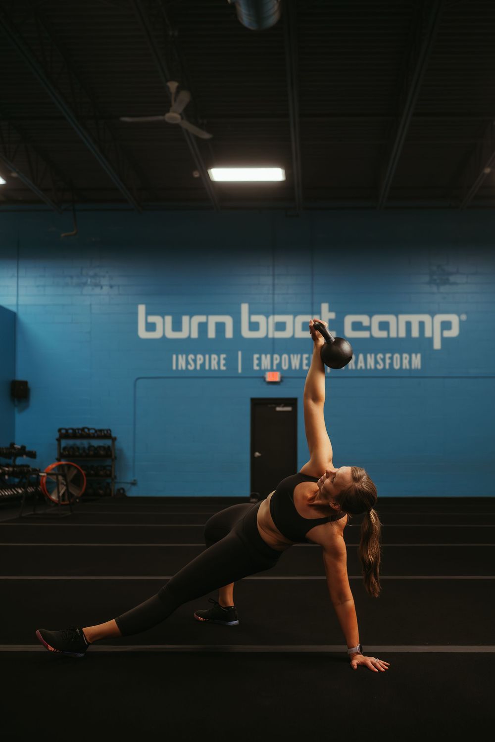 Athletic figure performs a side plank with raised arm at Burn Boot Camp fitness studio with blue wall background.