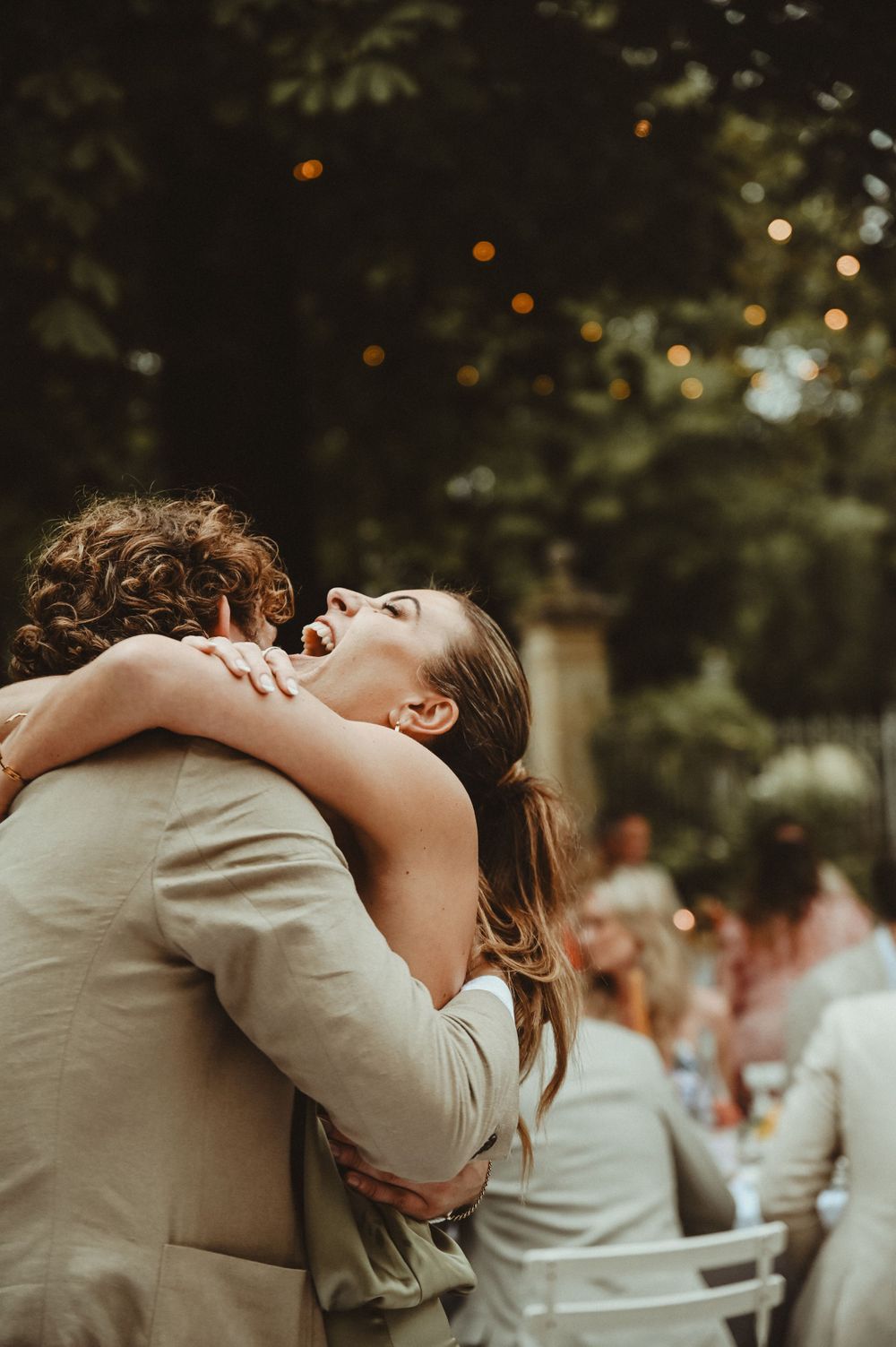 A romantic embrace between two people at an outdoor wedding celebration with bokeh lights in the background.