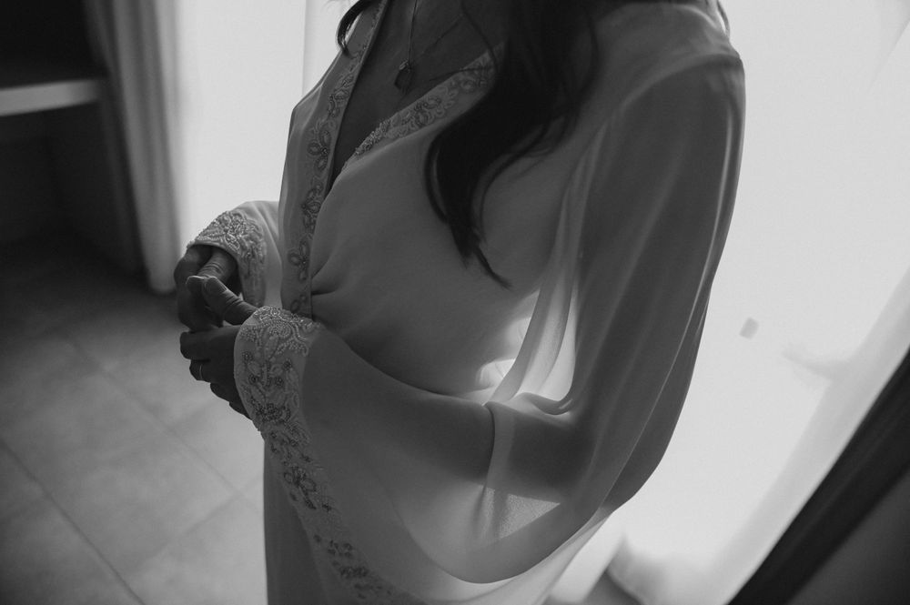 A black and white photograph captures a person in soft lighting wearing a light-colored blouse with delicate details.