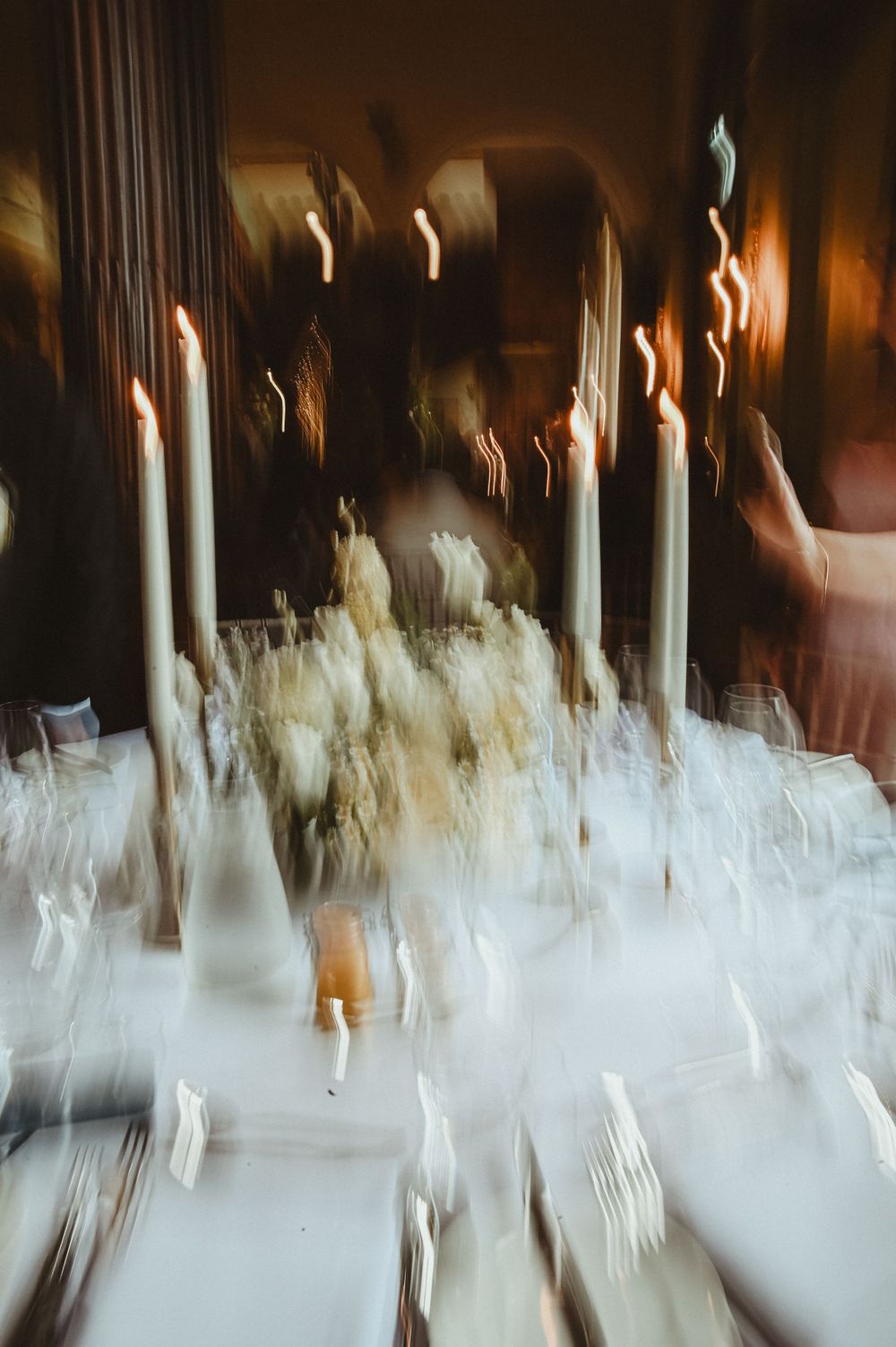 Blurred artistic photo of white candles and table settings with ethereal motion effect creating a dreamy atmosphere.