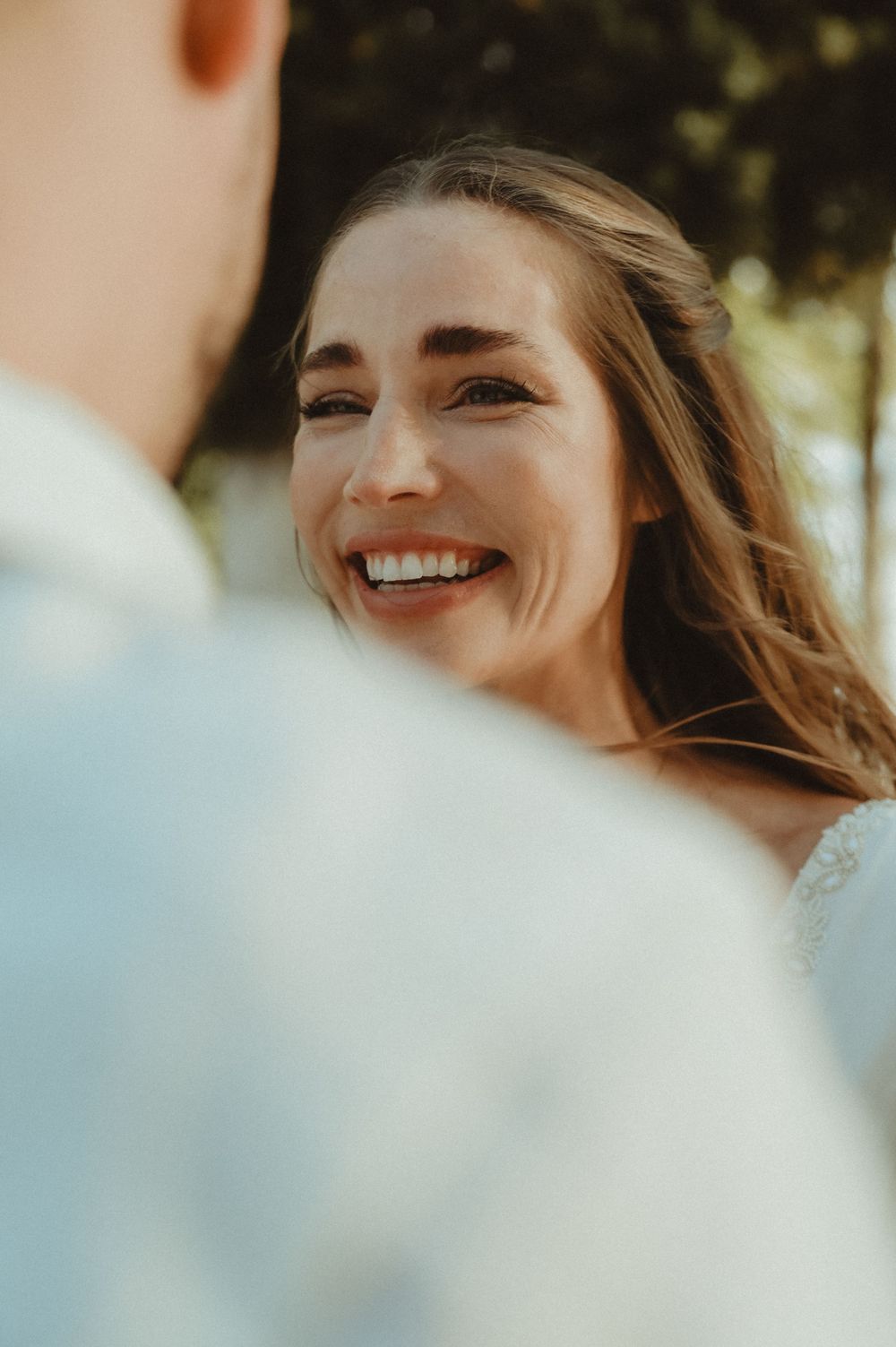 Warm close-up portrait shows radiant smile and flowing hair in dreamy outdoor sunlight.