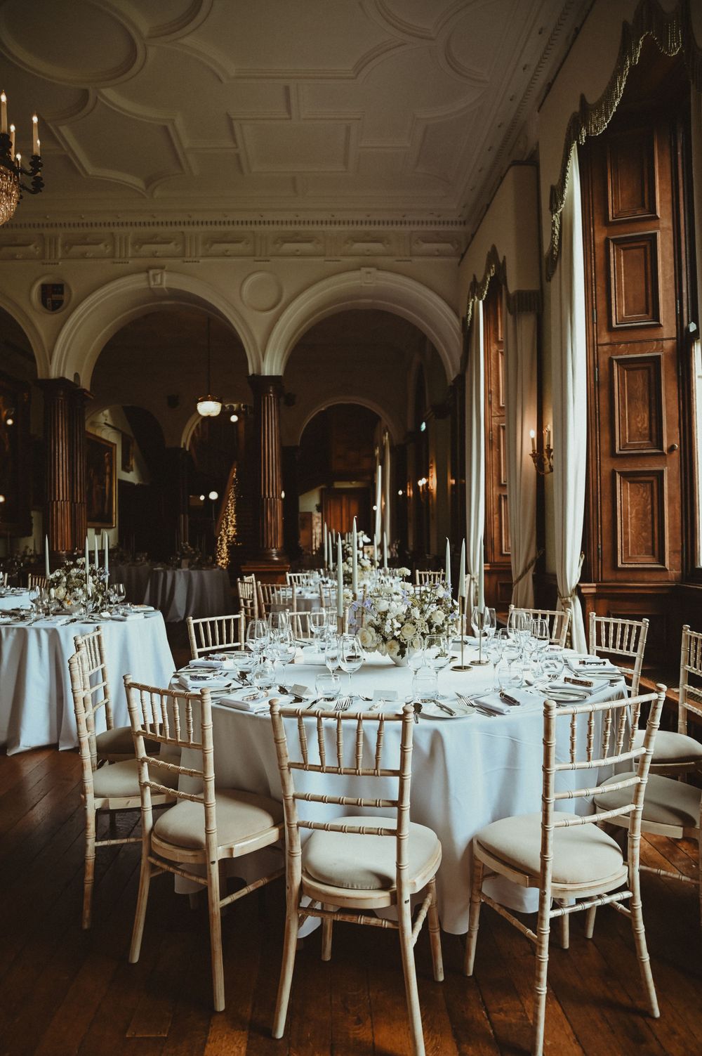 Elegant wedding reception hall with arched ceilings, white linens, and golden chiavari chairs set for dining.