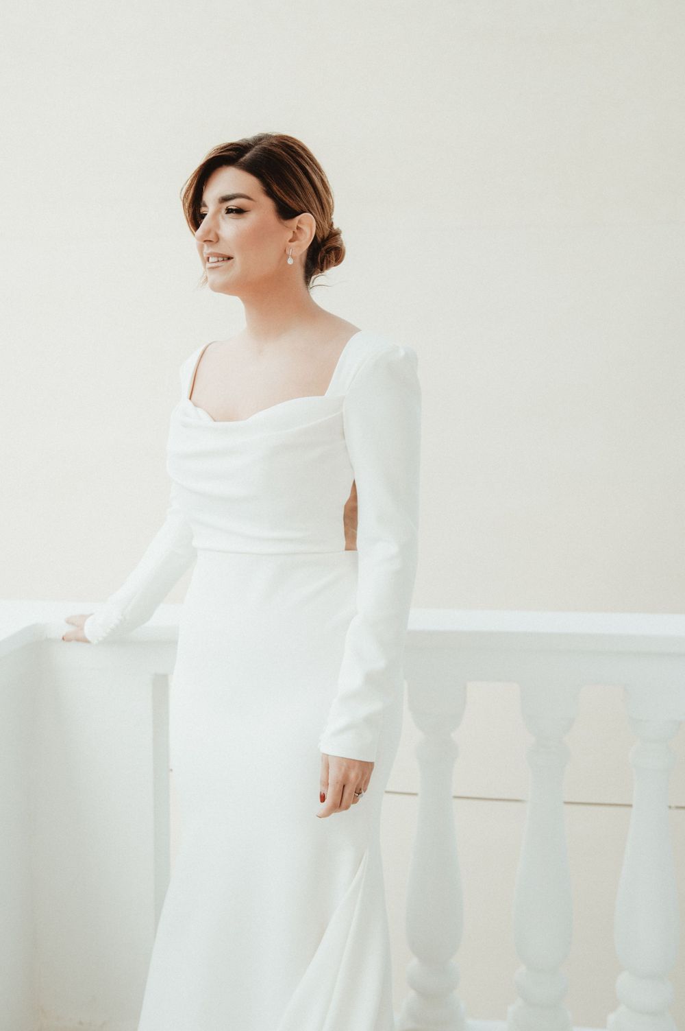 Portrait of person in elegant long-sleeved wedding dress with square neckline against white background.