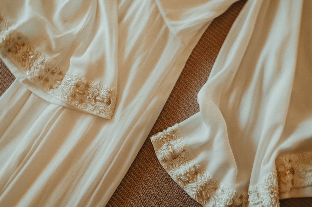Close-up detail of delicate lace trim on flowing white satin fabric against a textured background.