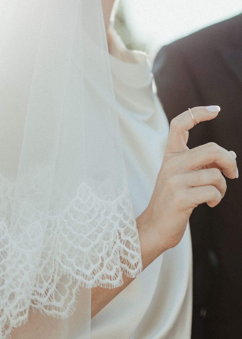 Close-up of a delicate white lace wedding veil with elegant scalloped trim and a hand gracefully lifting the fabric.