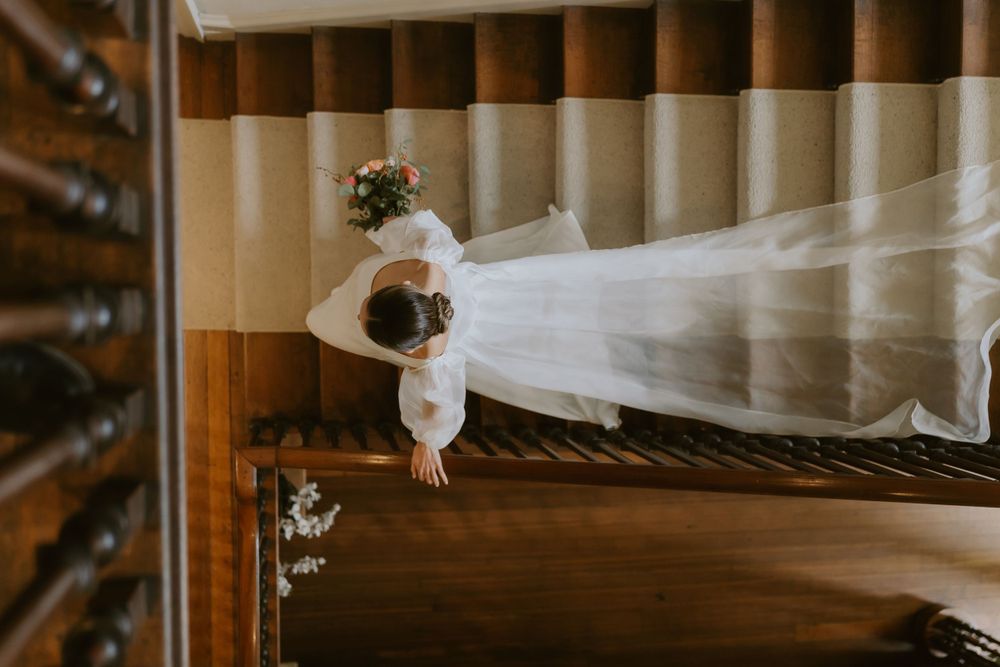 Flowing white wedding veil and dress against dark wooden floor in artistic top-down wedding photograph.