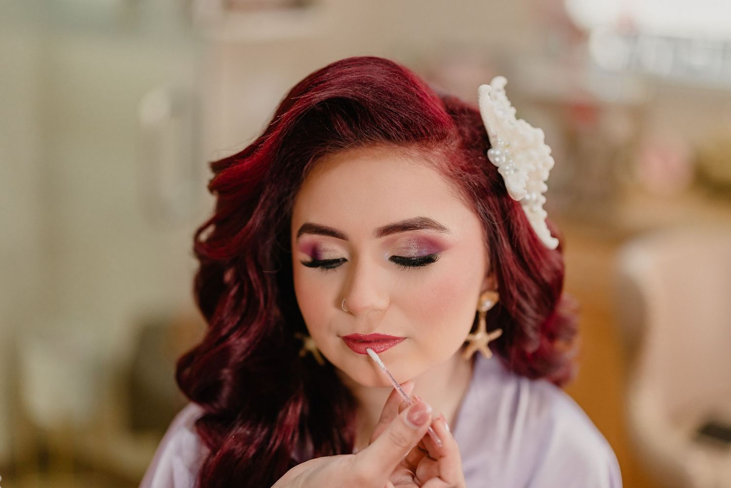 Close up beauty portrait of bride with burgundy red curled hair and soft glam makeup on wedding morning preparation.
