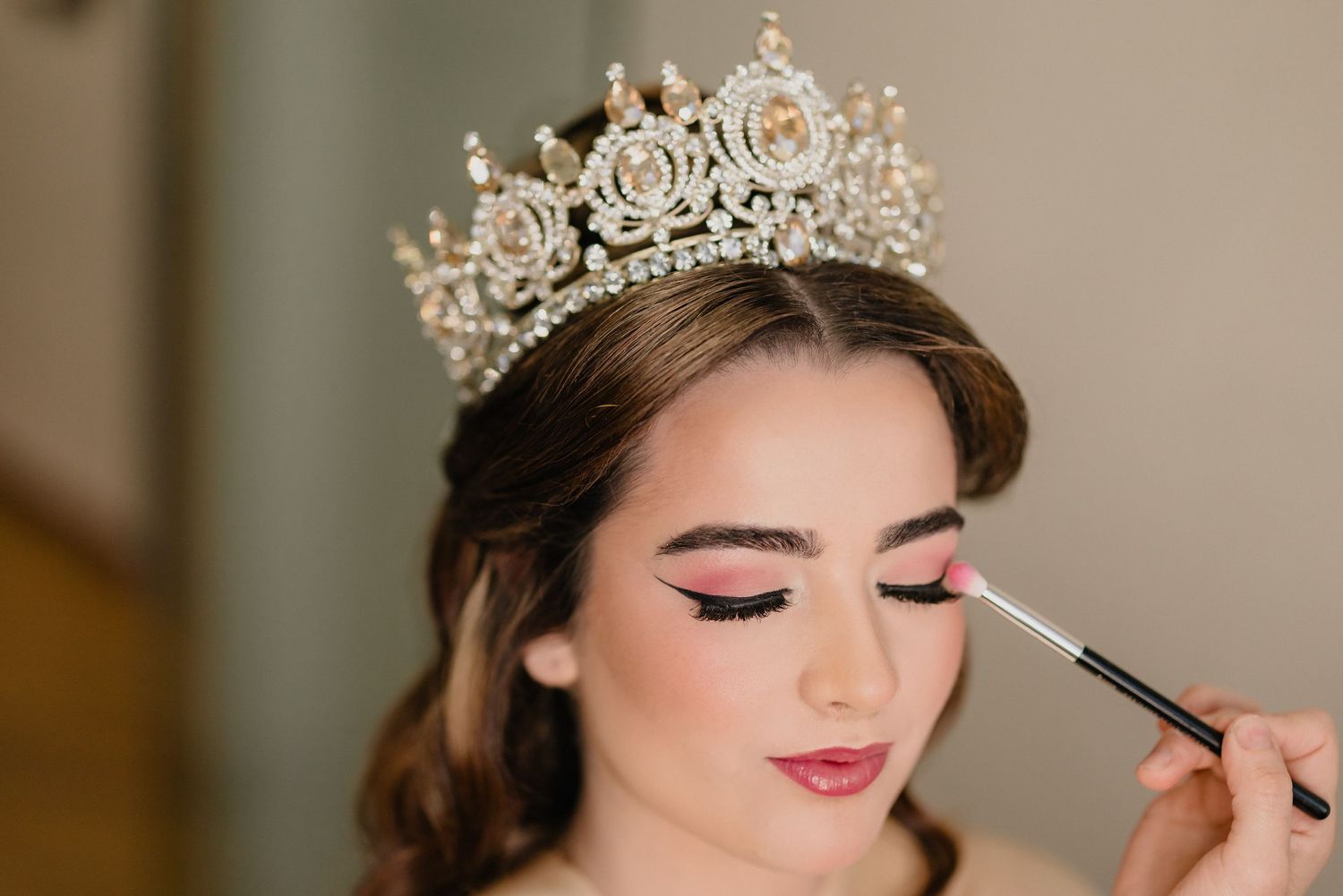 Professional makeup artist applying eye makeup on model wearing ornate silver crown.