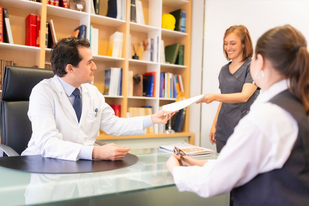 Medical professionals in white coats having a consultation meeting at a desk with bookshelves in the background.