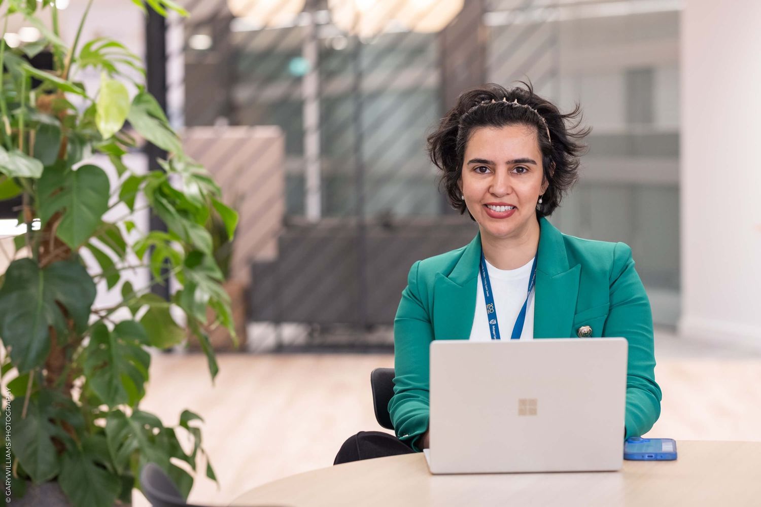 Professional woman in green blazer working on laptop in outdoor office setting.