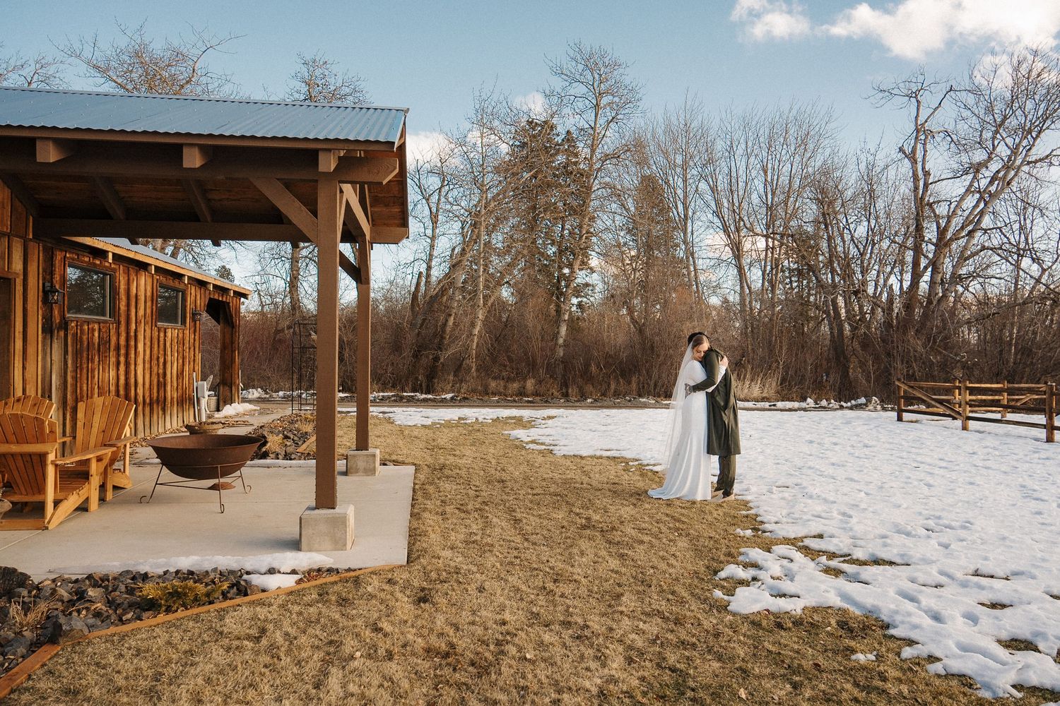 A rustic wooden cabin with a covered porch sits beside a snowy field during winter.