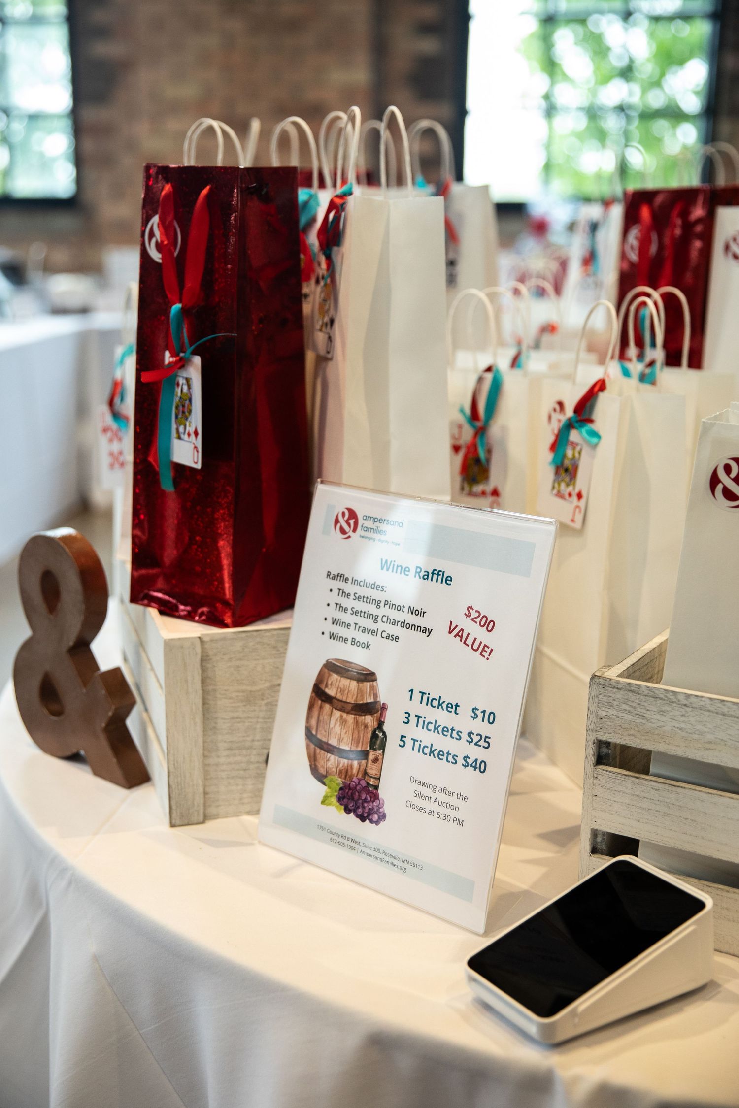 Gift bags with price signage and a mobile phone displayed on white tablecloth at an event check-in area.