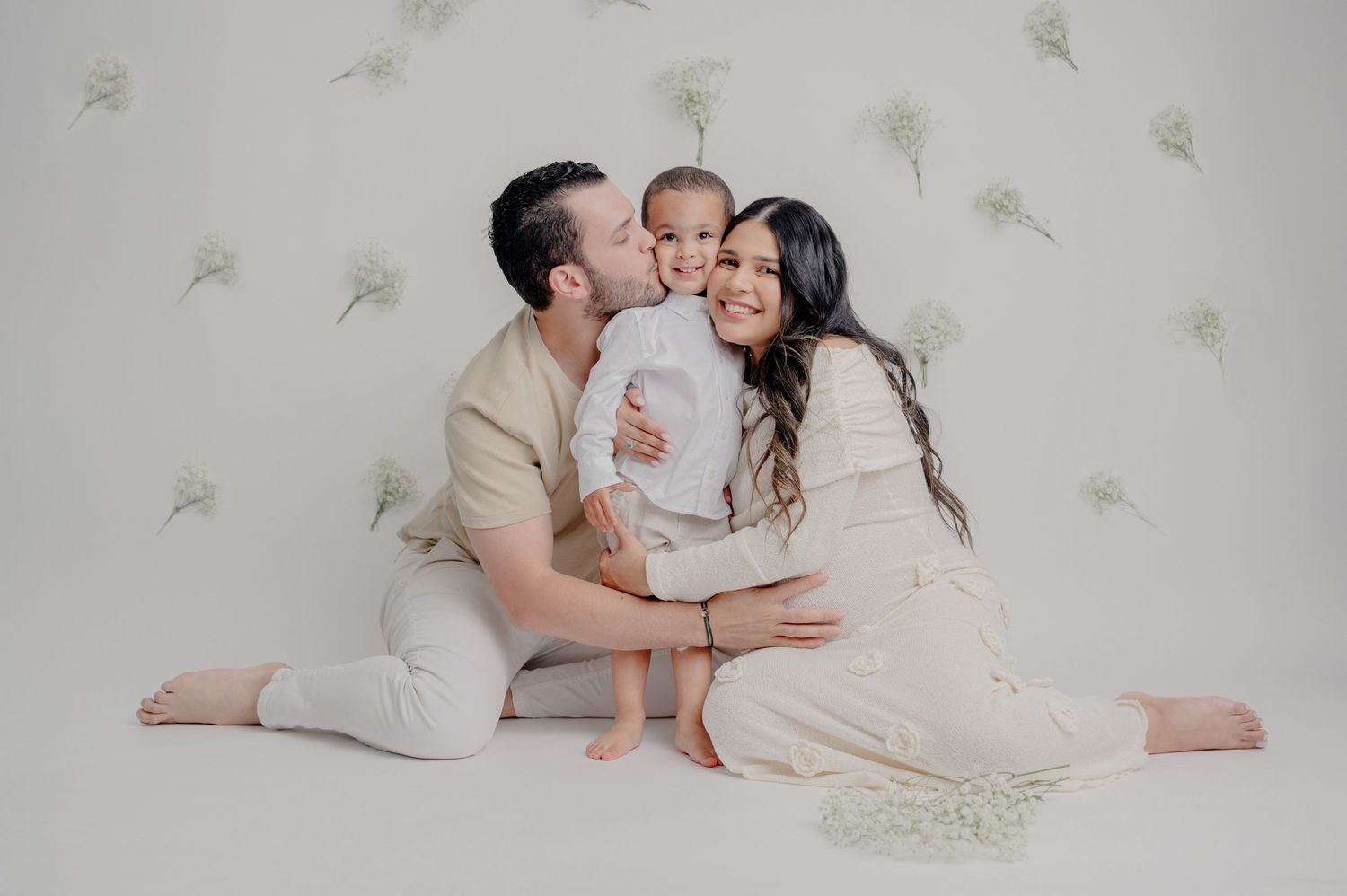 Three people in light colored outfits sit together on white backdrop with delicate floating feather pattern.