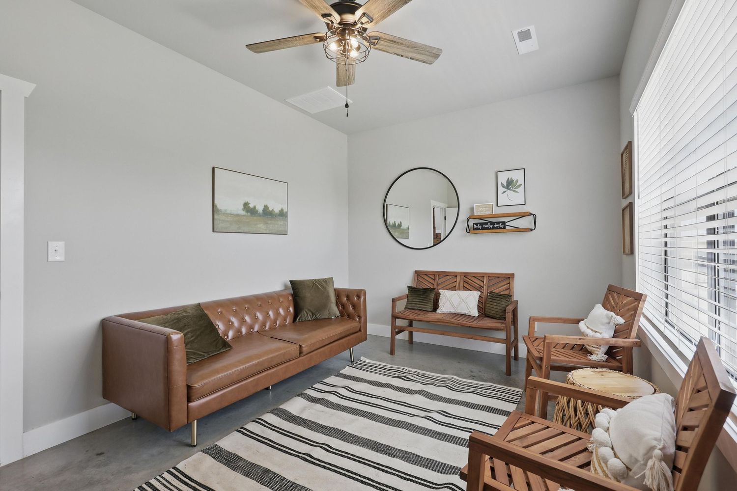 Cozy living room with leather sofa, striped area rug, circular mirrors, and natural light from large window.