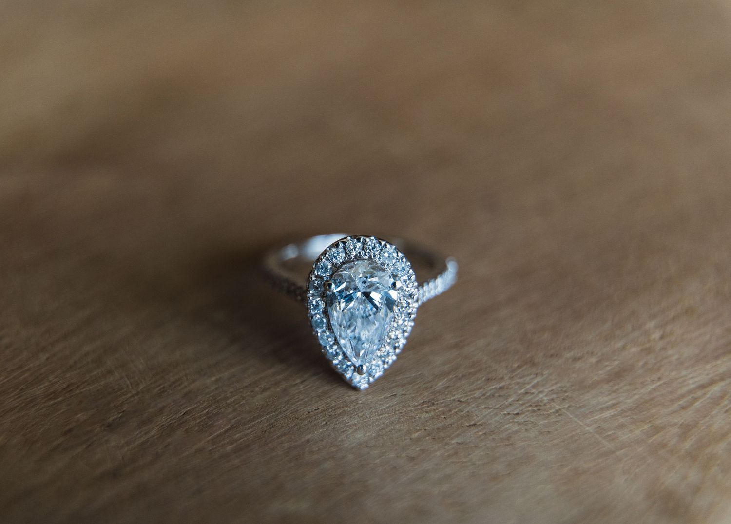 Elegant pear-shaped diamond halo engagement ring resting on wooden surface in natural light.