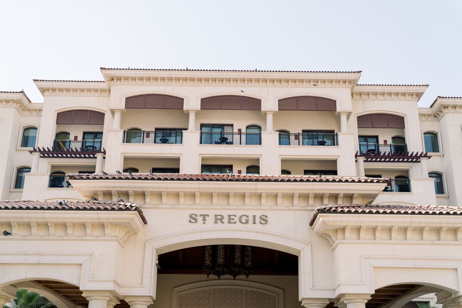 Elegant white St. Regis hotel exterior featuring Mediterranean-style architecture with multiple balconies and archways.